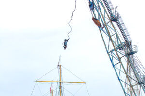 two people doing bungee jumping from crane in front of sailing ship